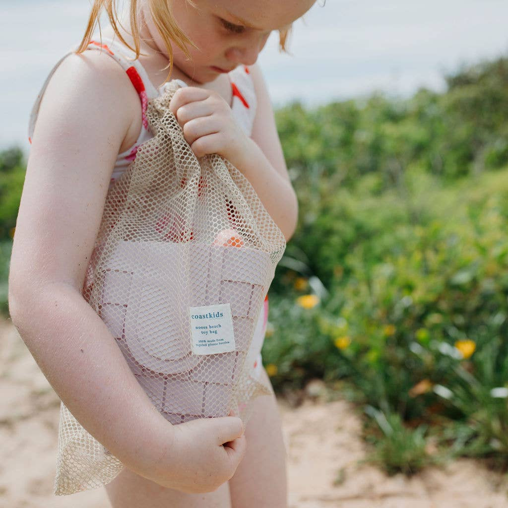 young girl holding a mesh bag on a beach